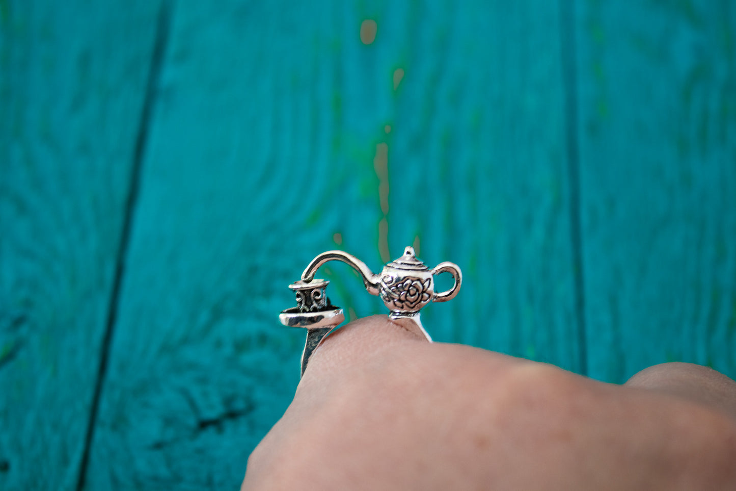 Silver teapot charm on a ring against a teal background